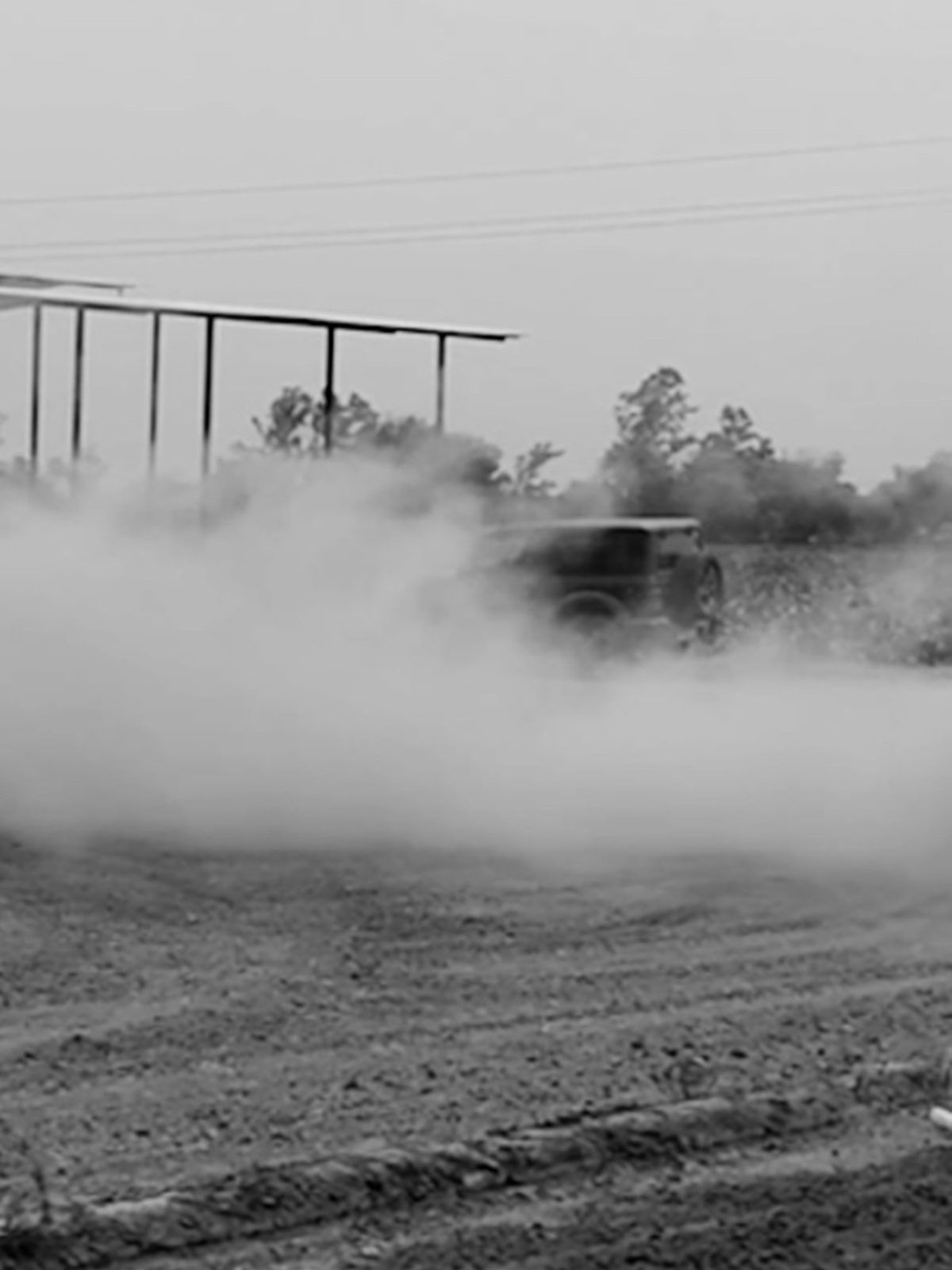 Car doing a burnout with smoke on a dirt lot, black and white