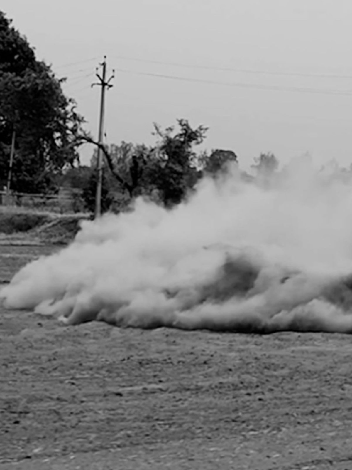 Burnout smoke cloud trailing across a field, black and white